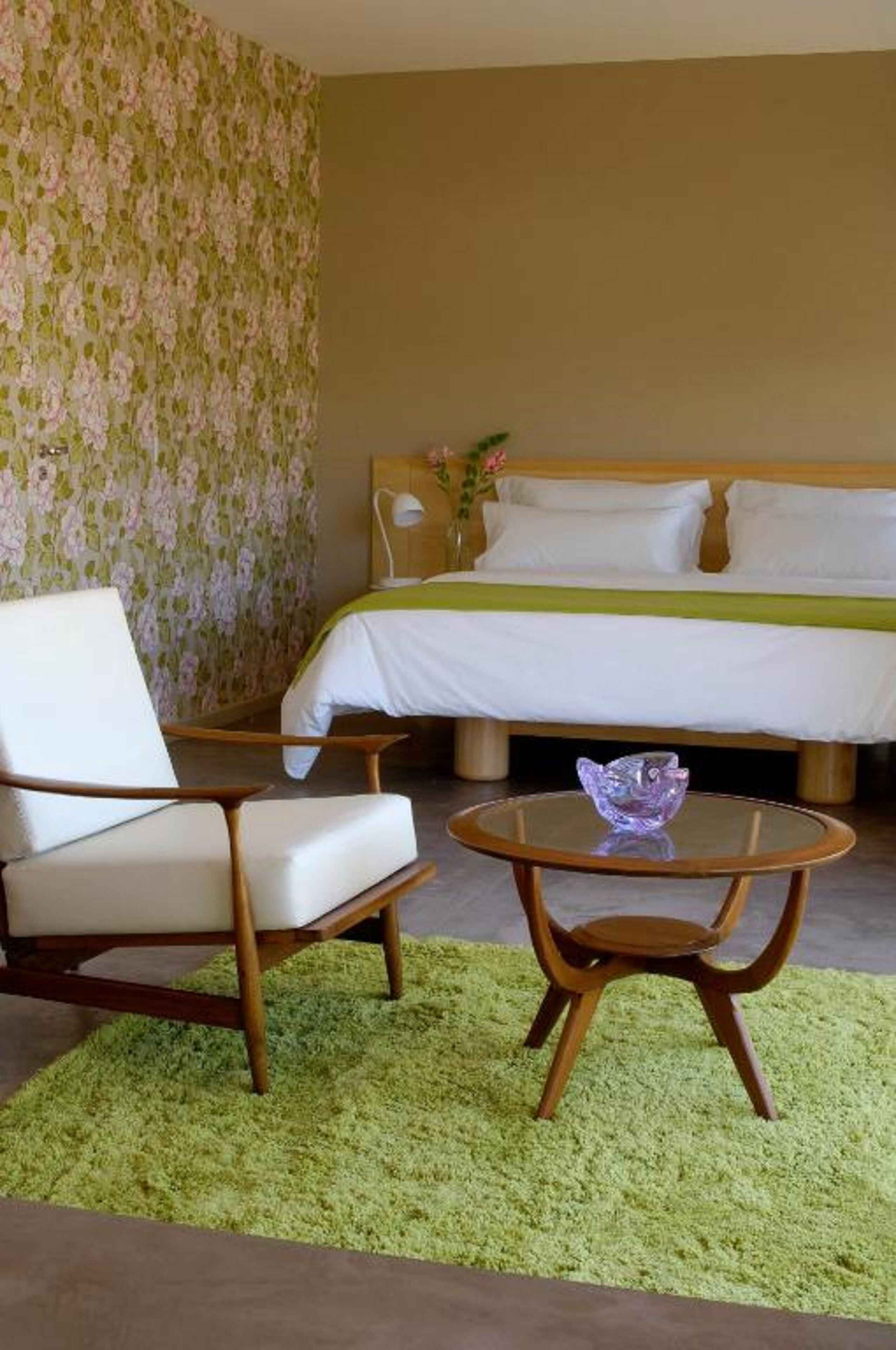 Una habitación de hotel con una cama, una silla, una mesita y una alfombra verde.