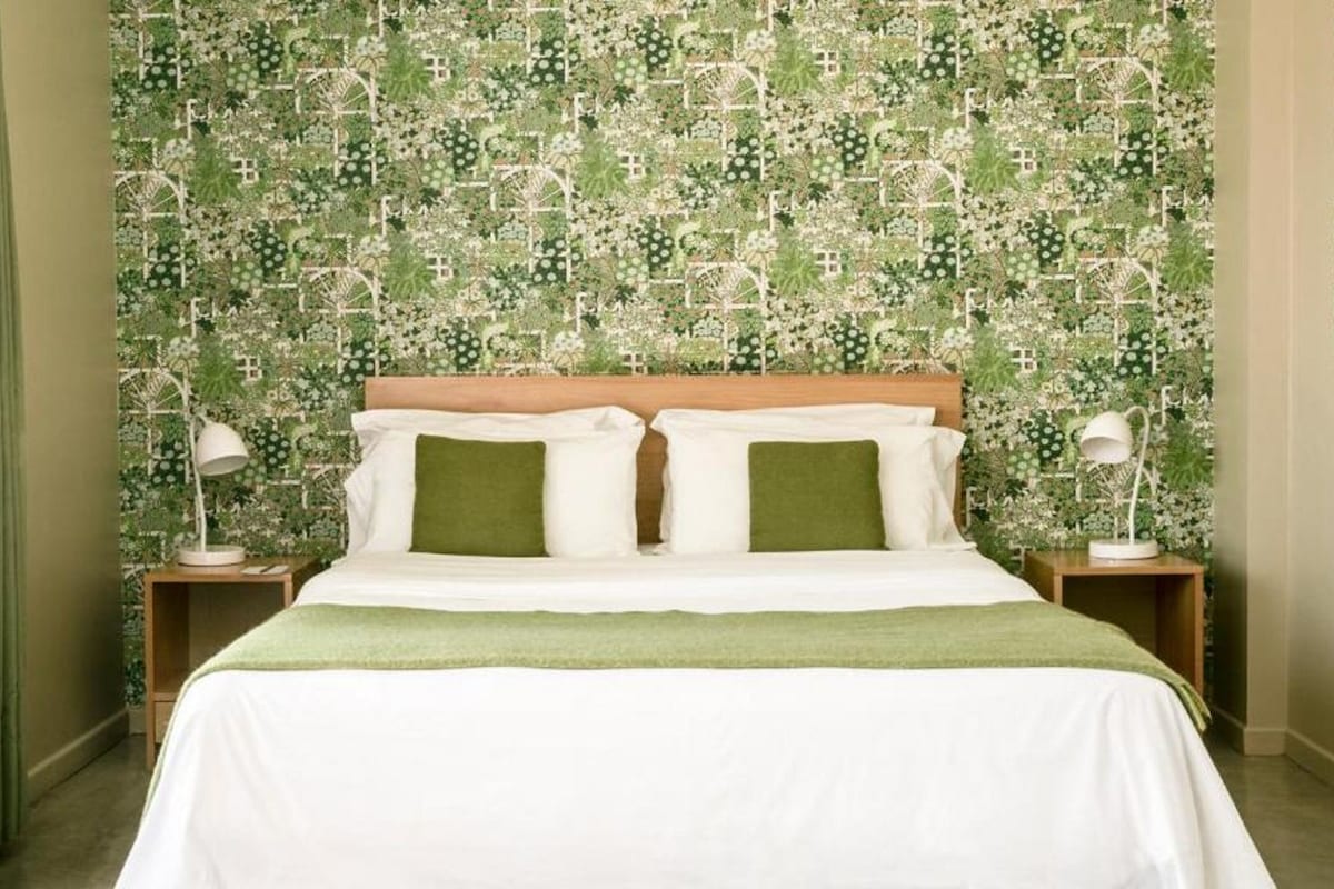 A bedroom with a bed, two bedside tables, and a green patterned wallpaper.