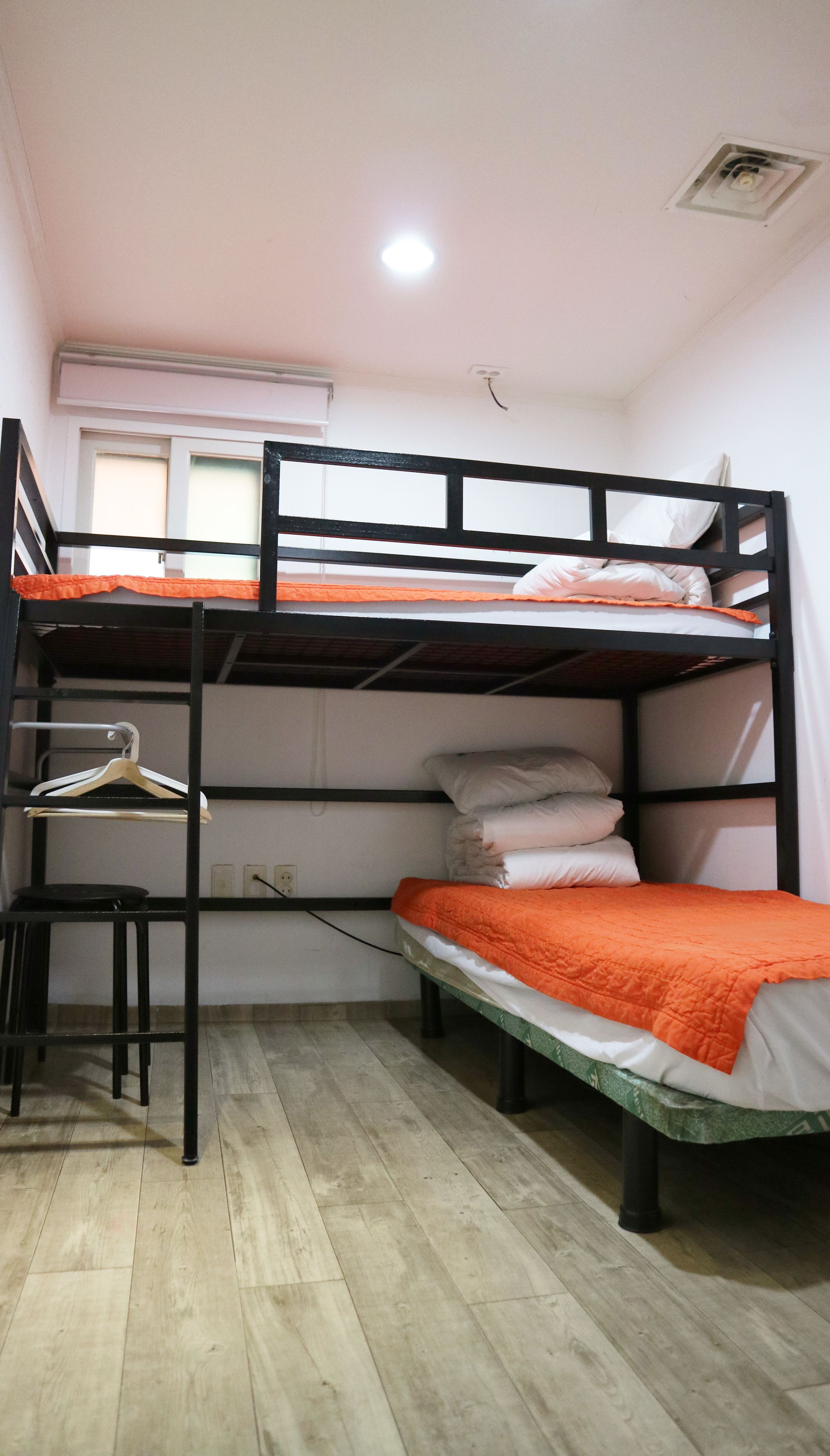 A bunk bed room with a desk and chair, a hanging light fixture, and a window with blinds.