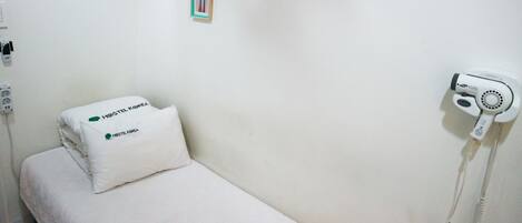 Een schone, minimalistisch ingerichte kamer met een bed, een kussen, een haardroger en een klein fotokader aan de muur.