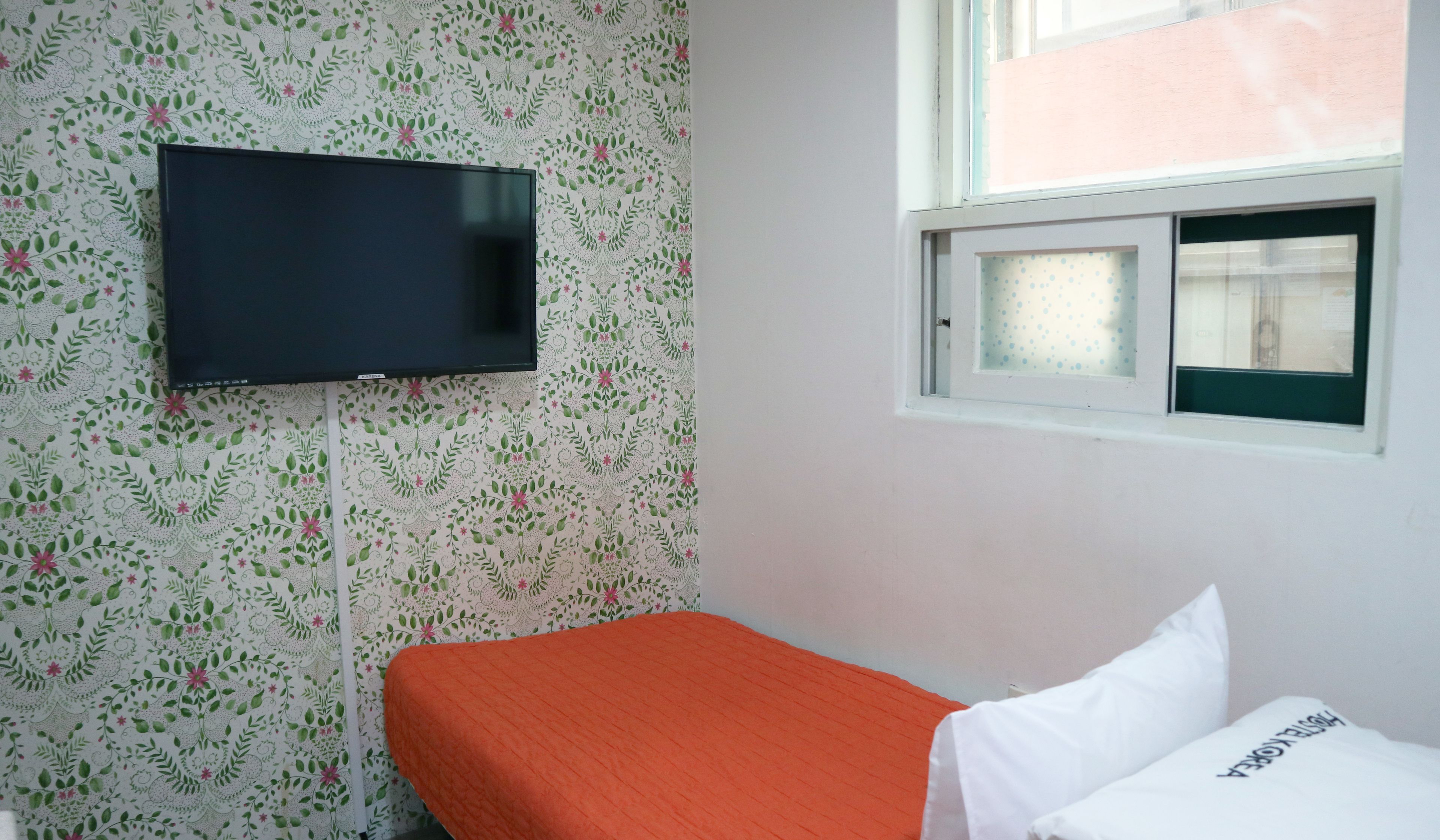 A room with a bed, a television mounted on the wall, and a window with a view of the outside.