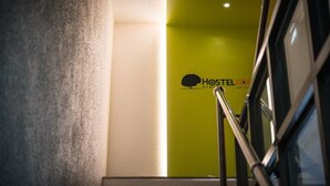 Una escalera conduce a una habitación con una pared verde y el logotipo de Hostel.