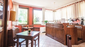Een keuken met houten kastjes, een eettafel met stoelen, een raam met gordijnen en een radiator.
