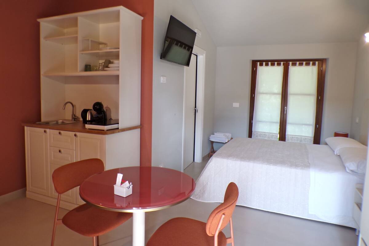 Une chambre d’hôtel comprenant un lit, un téléviseur fixé au mur, une kitchenette et une petite table avec des chaises.
