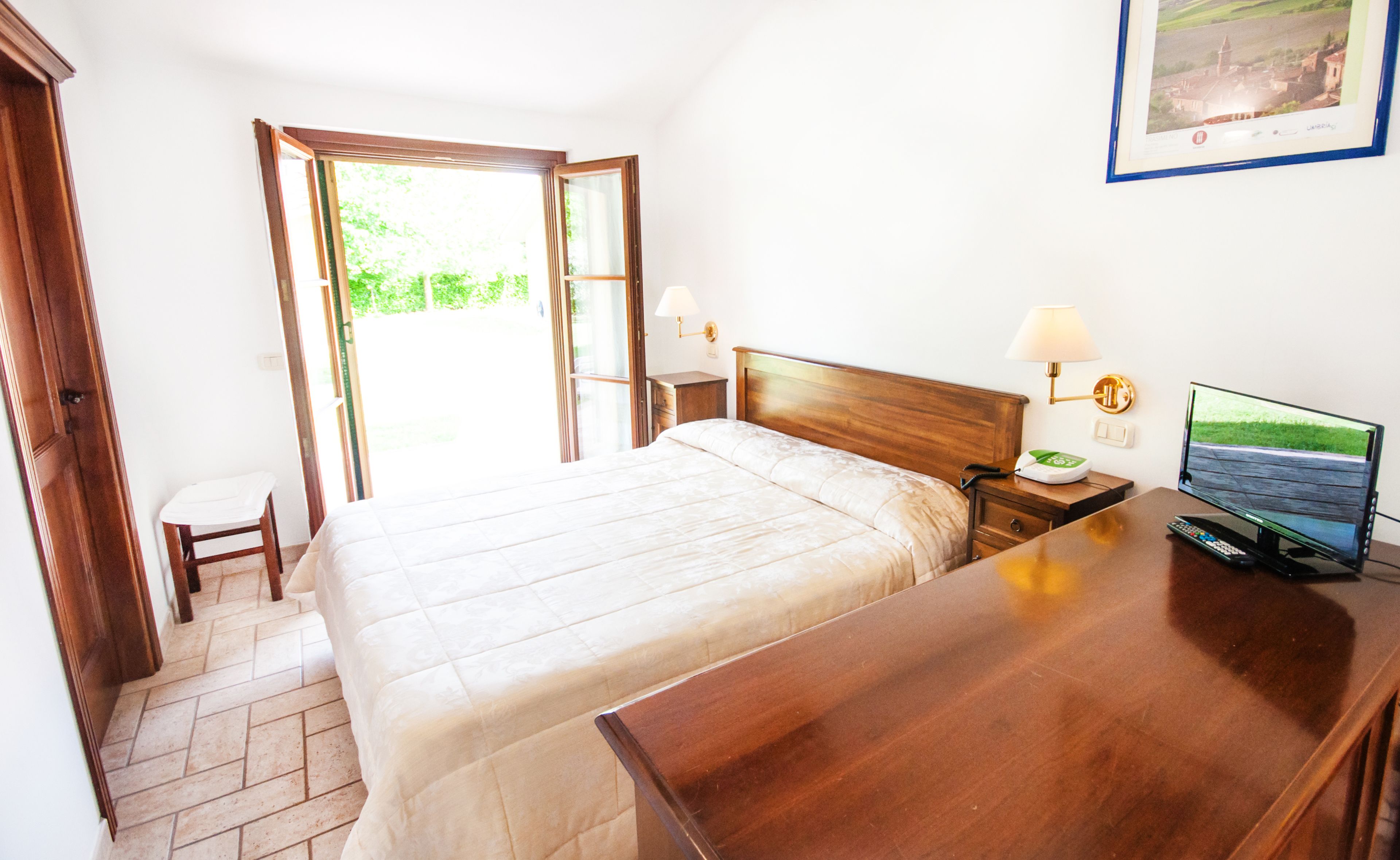 A hotel room with a bed, bedside table, lamp, and a television.