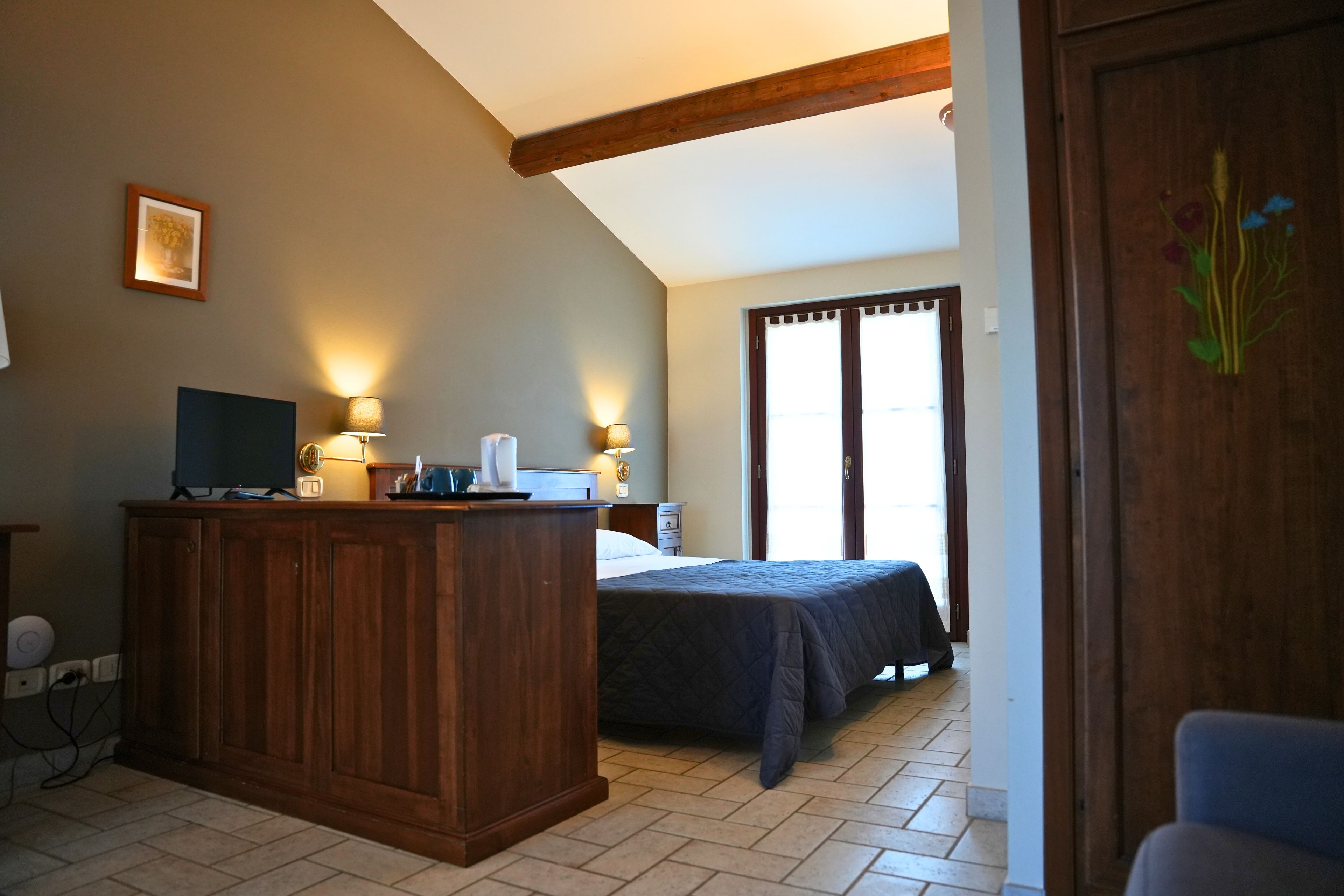 A hotel room with a wooden desk, a bed, and a large window with curtains.