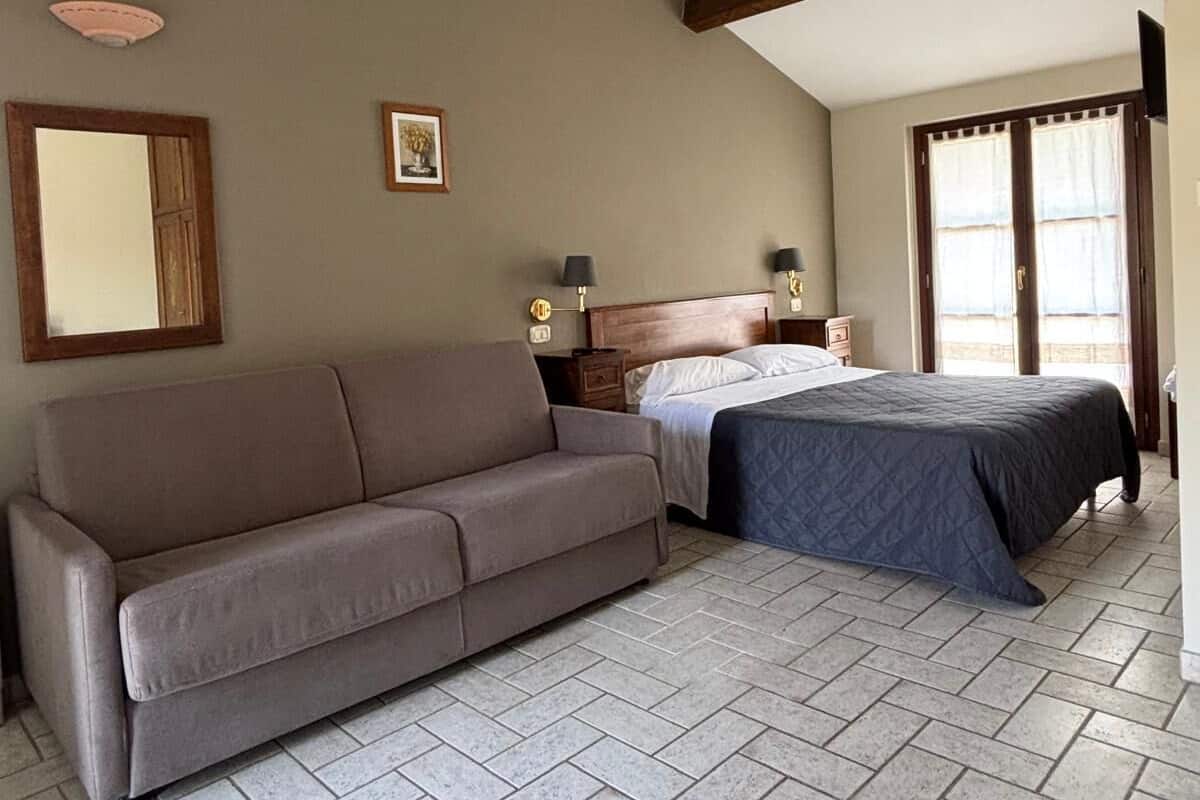 Une chambre à coucher avec un canapé, un lit, une table de chevet, une lampe et une fenêtre avec des rideaux.