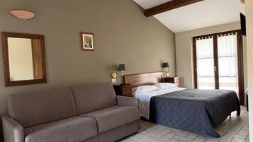 Una camera da letto con un divano, un letto, un comodino, una lampada e una finestra con tende.