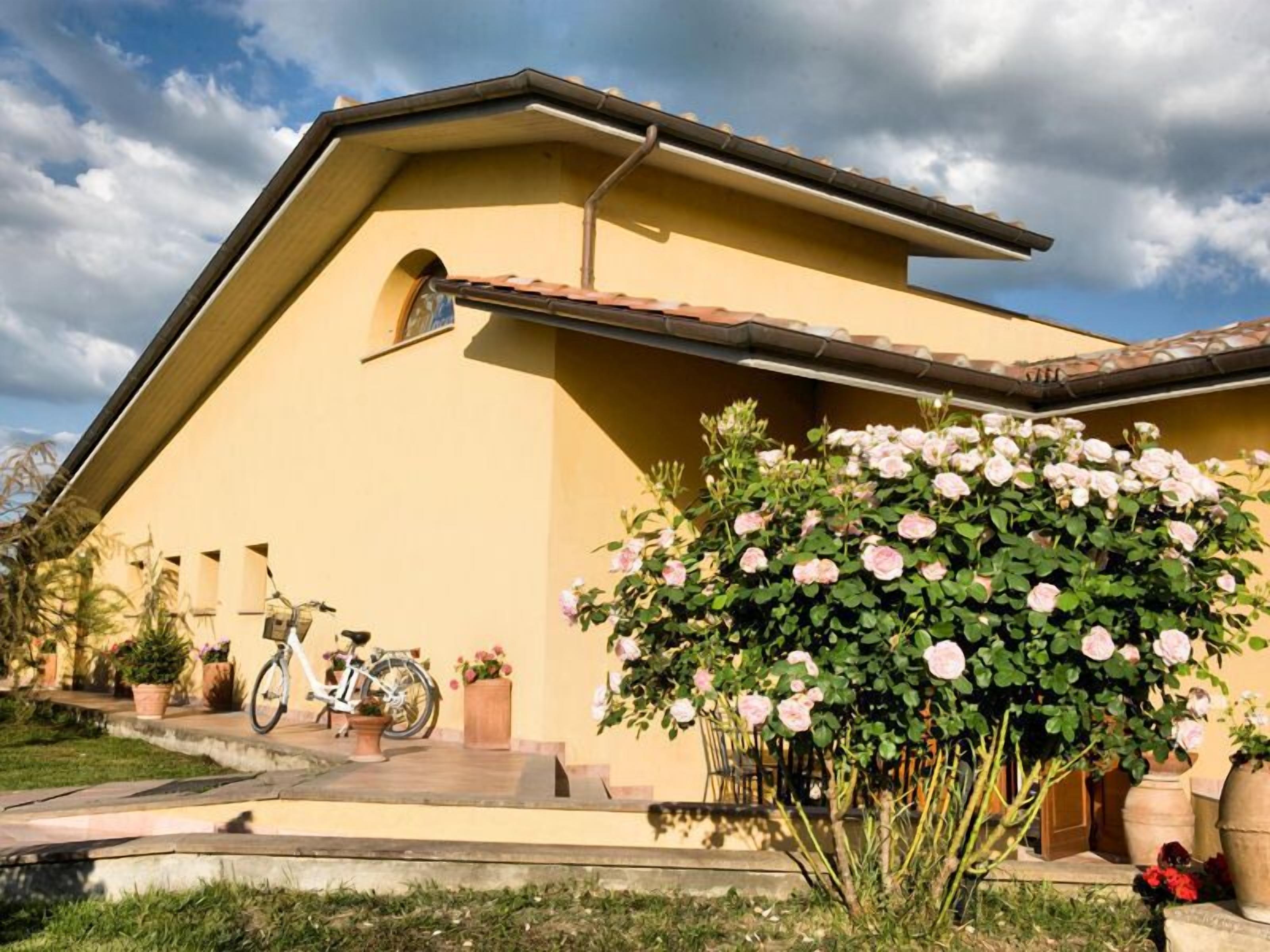 A yellow building with a sloped roof, a bicycle parked outside, and a large bush of pink roses.
