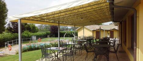 An outdoor patio area with tables and chairs, a pool, and a covered seating area.