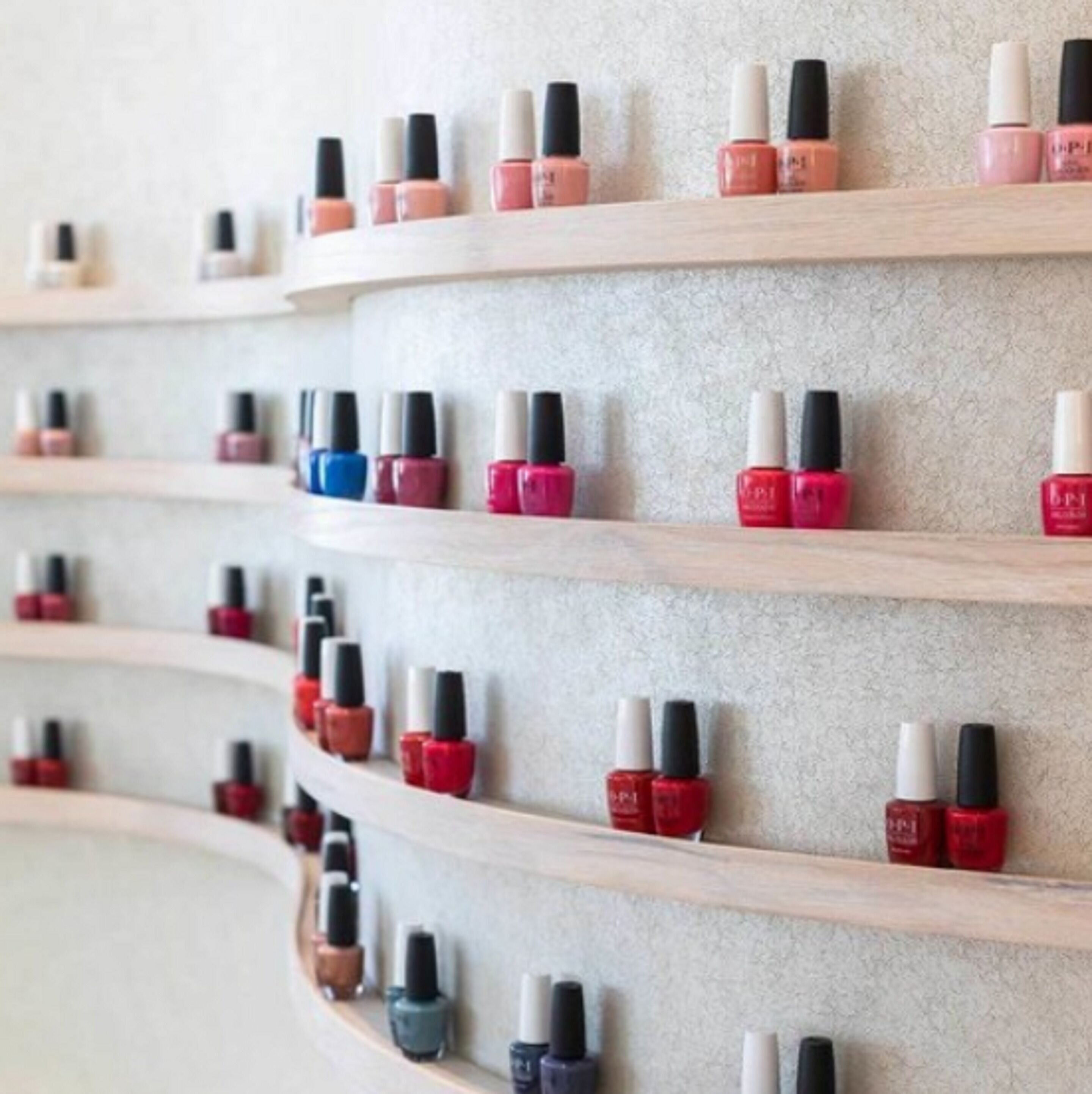 A wall with multiple shelves displaying various nail polish bottles.
