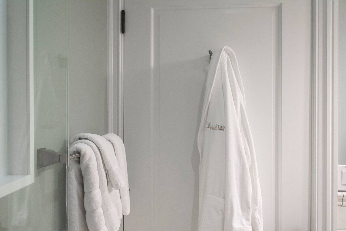 A bathroom with a glass shower enclosure, a white towel rack, and a white robe hanging on the door.