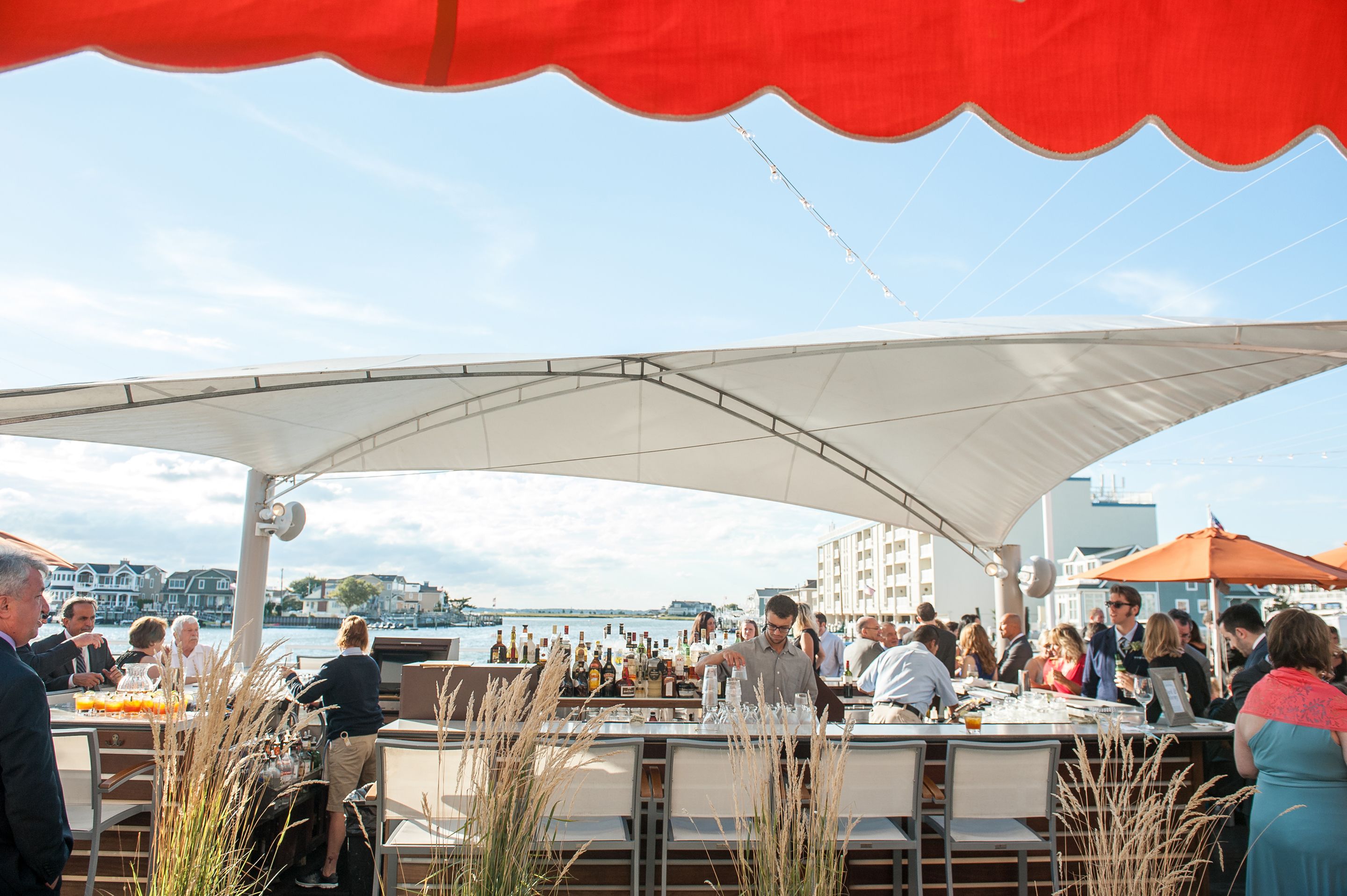 An outdoor dining area with tables and chairs, a bar, and a view of the water.