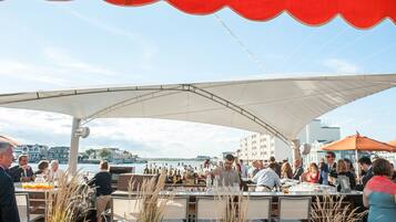 An outdoor dining area with tables and chairs, a bar, and a view of the water.