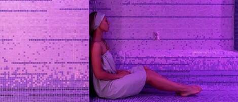 A person sitting on a textured, purple-hued surface with a patterned wall in the background.