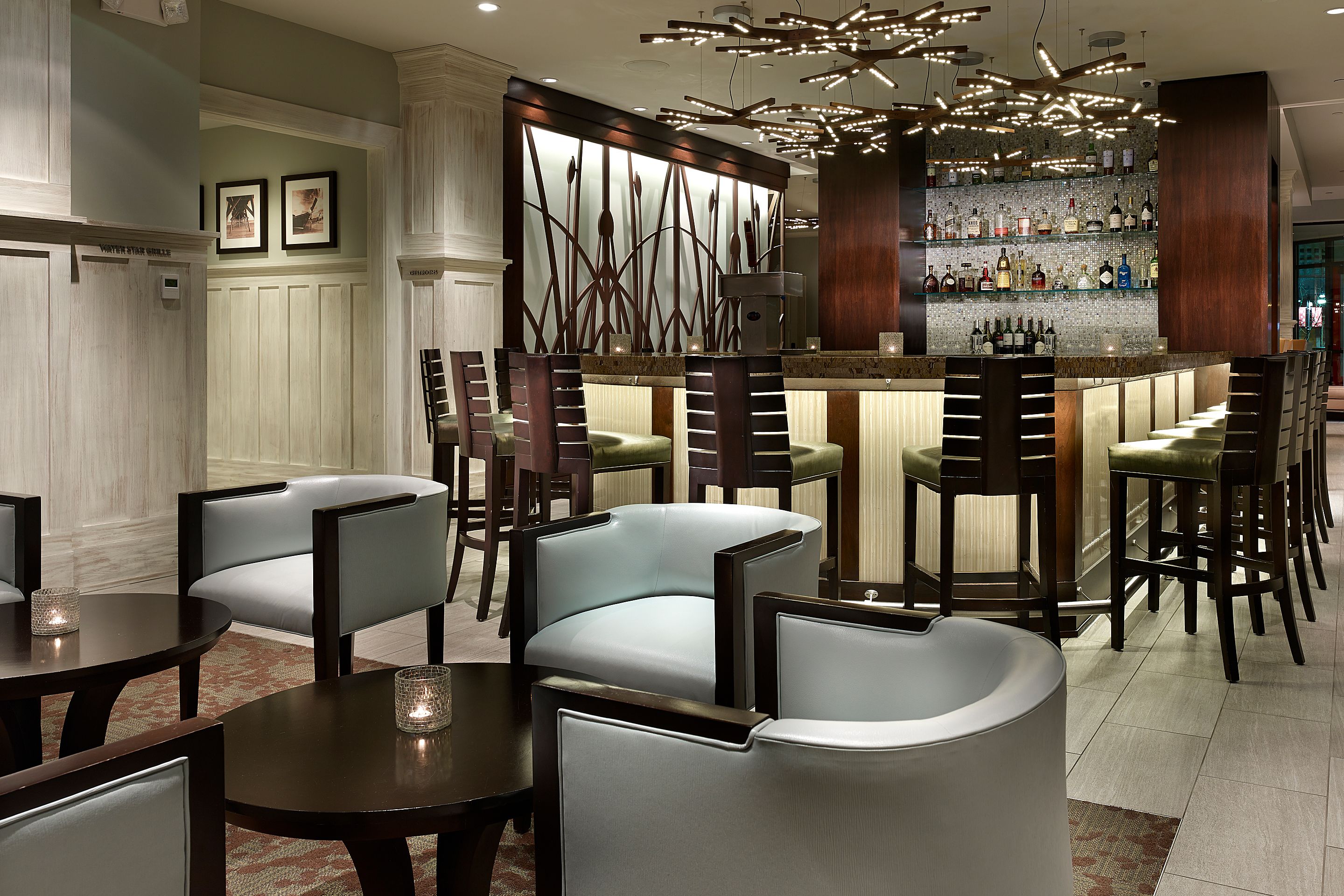 A bar area with a modern design, featuring a bar counter, multiple seating options, and a decorative wall with framed pictures.
