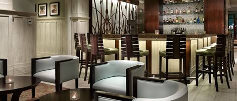 A bar area with a modern design, featuring a bar counter, multiple seating options, and a decorative wall with framed pictures.