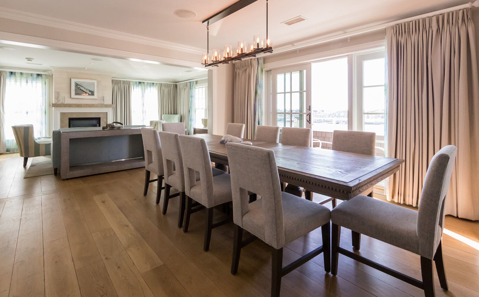 A spacious dining area with a long wooden table and six chairs, a fireplace, and a large window with curtains.
