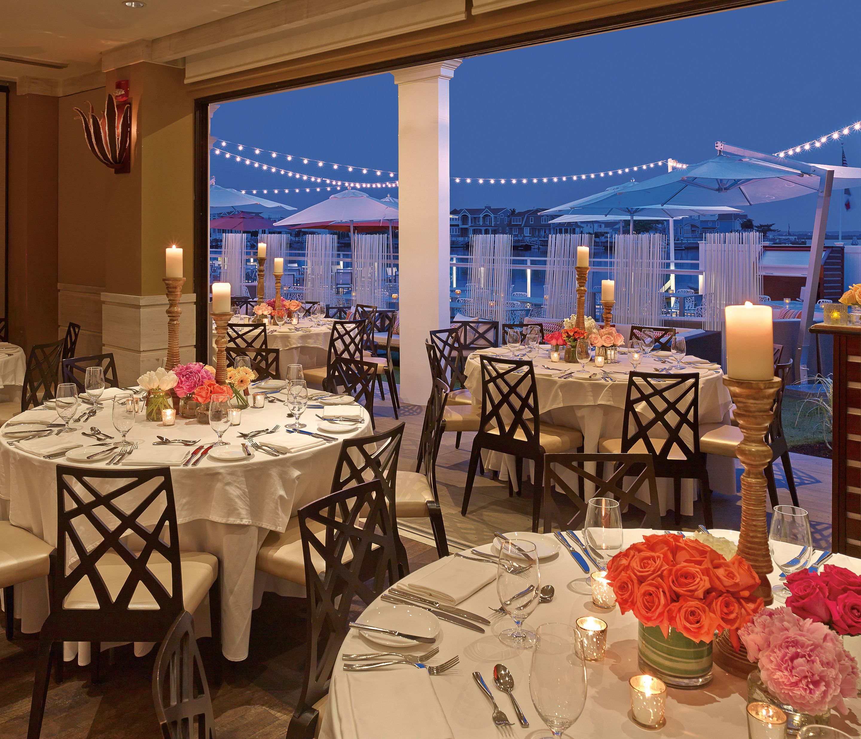 A restaurant with round tables set for dining, featuring white tablecloths, candles, and floral centerpieces.