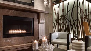 A modern living room with a fireplace, a comfortable chair, a table with books, and decorative candles. - The Reeds at Shelter Haven (Stone Harbor)