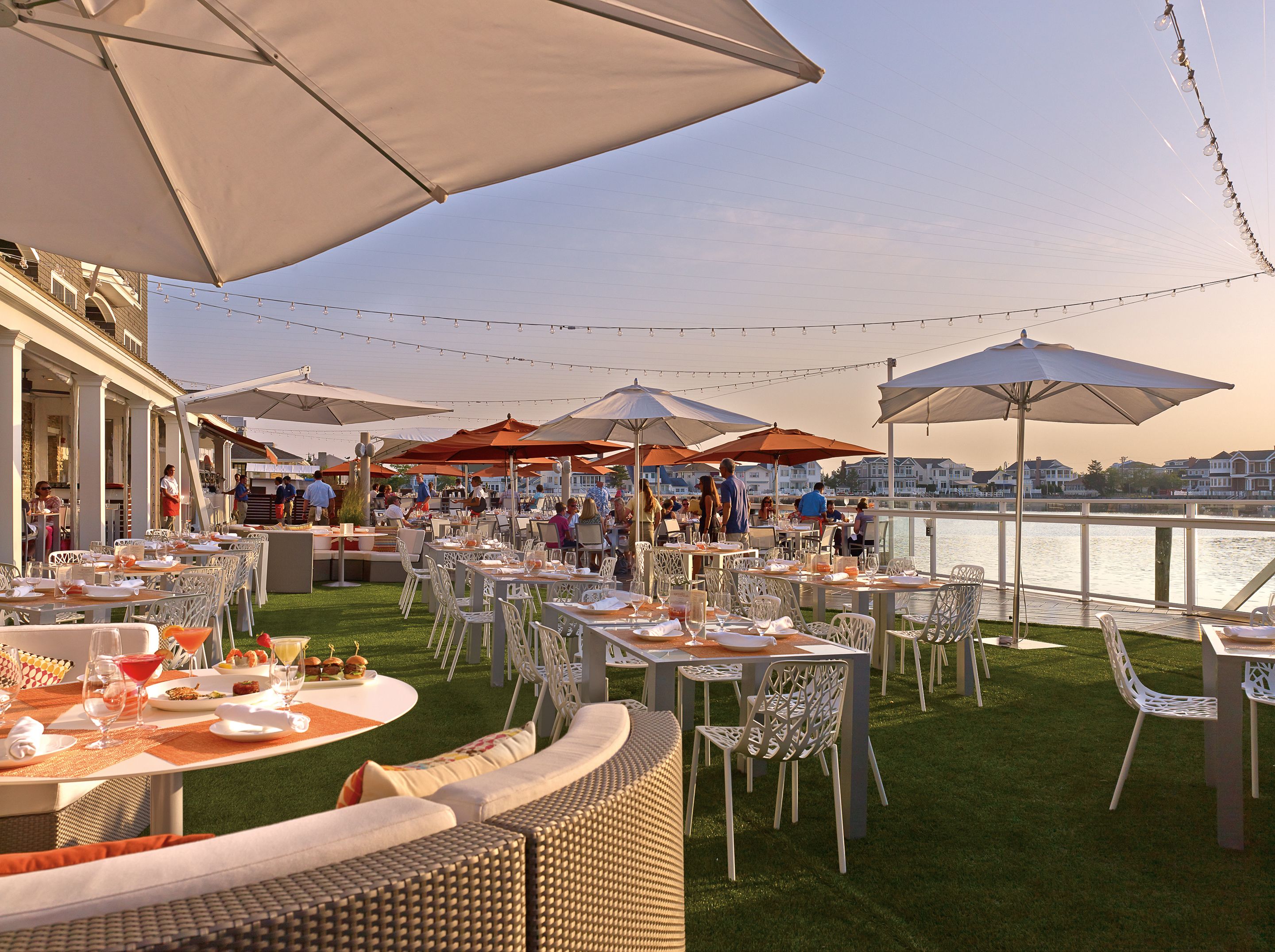 An outdoor dining area with tables and chairs, umbrellas, and a view of the water.