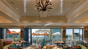 A dining area with tables set for meals, a large chandelier, and a view of the outdoors. - The Reeds at Shelter Haven (Stone Harbor)