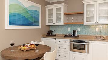 A modern kitchen with white cabinetry, a dining table with chairs, a coffee maker, and a large abstract painting on the wall.