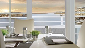 A table set for two with a view of the waterfront and buildings across the water. - The Reeds at Shelter Haven (Stone Harbor)