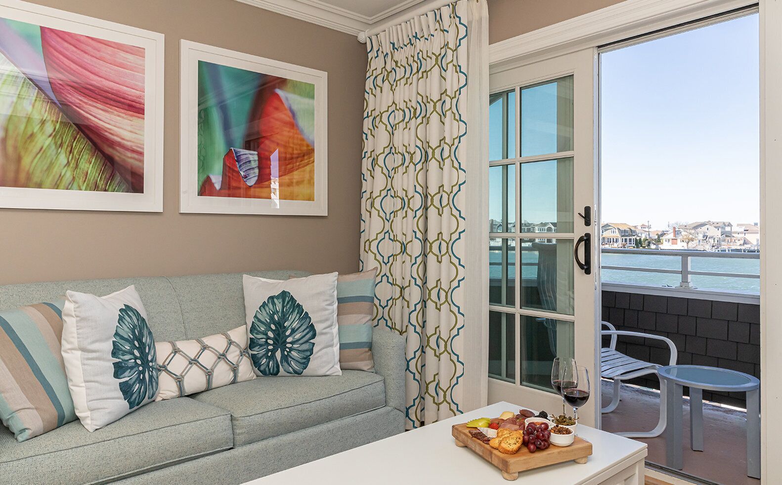 A living room with a grey sofa, a coffee table with a fruit platter, and a view of the sea through a window.