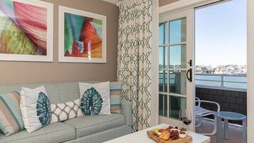 A living room with a grey sofa, a coffee table with a fruit platter, and a view of the sea through a window.