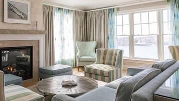 Una sala de estar moderna con chimenea, sillones a rayas, un sofá y vistas a una masa de agua a través de amplias ventanas.