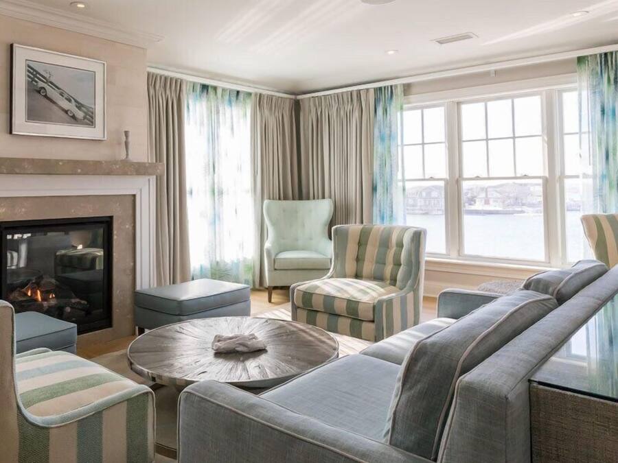 Una sala de estar moderna con chimenea, sillones a rayas, un sofá y vistas a una masa de agua a través de amplias ventanas.