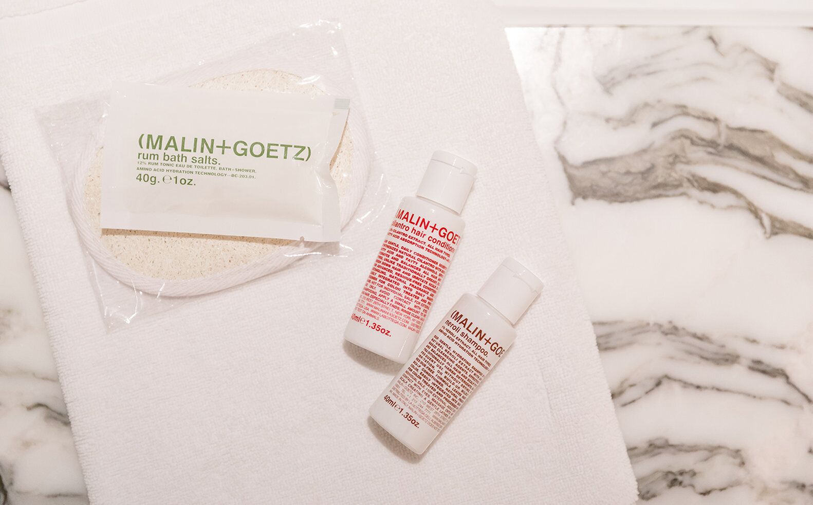 A bathroom with a marble countertop, containing a package of bath salts and two bottles of hair conditioner and shampoo.