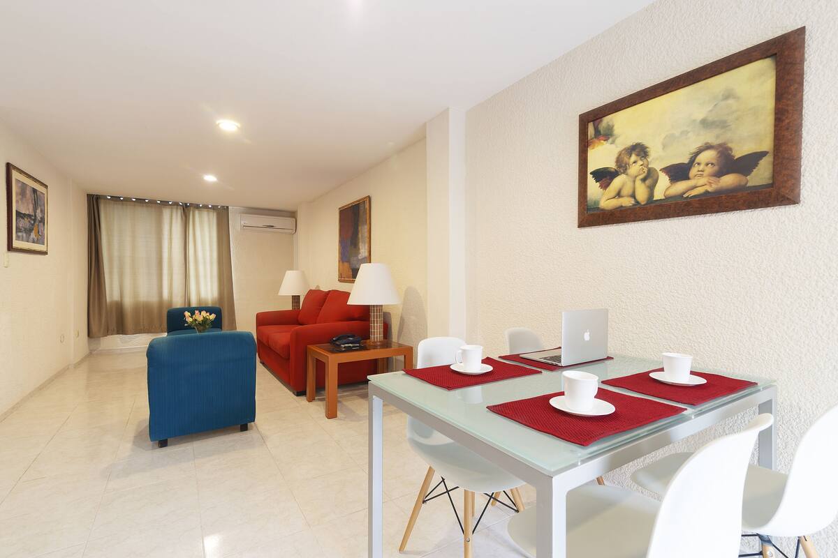 A modern hotel room with a dining area, a sofa, a coffee table, and a painting on the wall.