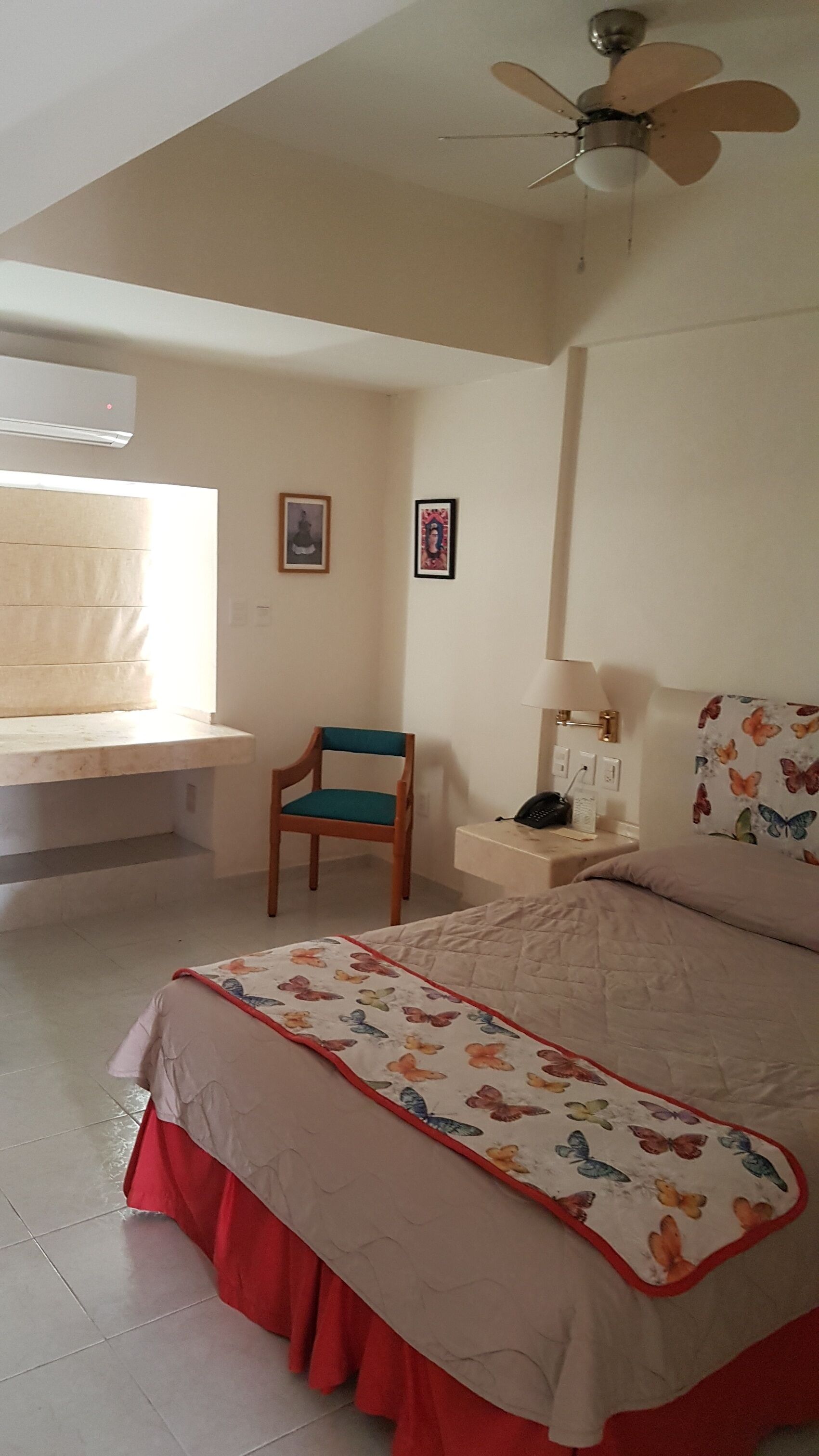 A bedroom with a bed, a chair, a bedside table with a lamp, and a ceiling fan.