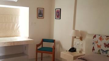 A bedroom with a bed, a chair, a bedside table with a lamp, and a ceiling fan.