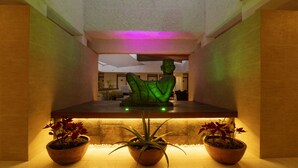 A reception area with a green illuminated sculpture, a reception desk, and potted plants. - Hotel & Suites Nader (Cancun)