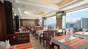 Un restaurant amb taules preparades per dinar, una zona de bar i grans finestres que ofereixen vista a la ciutat.