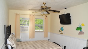 A bedroom with a bed, a ceiling fan, a television mounted on the wall, and a window with curtains. - Conch On Inn Motel (Tavernier)