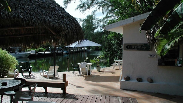 A wooden deck with outdoor seating, a thatched roof structure, a small building labeled 'OFFICE', and a body of water in the background. - Conch On Inn Motel (Tavernier)
