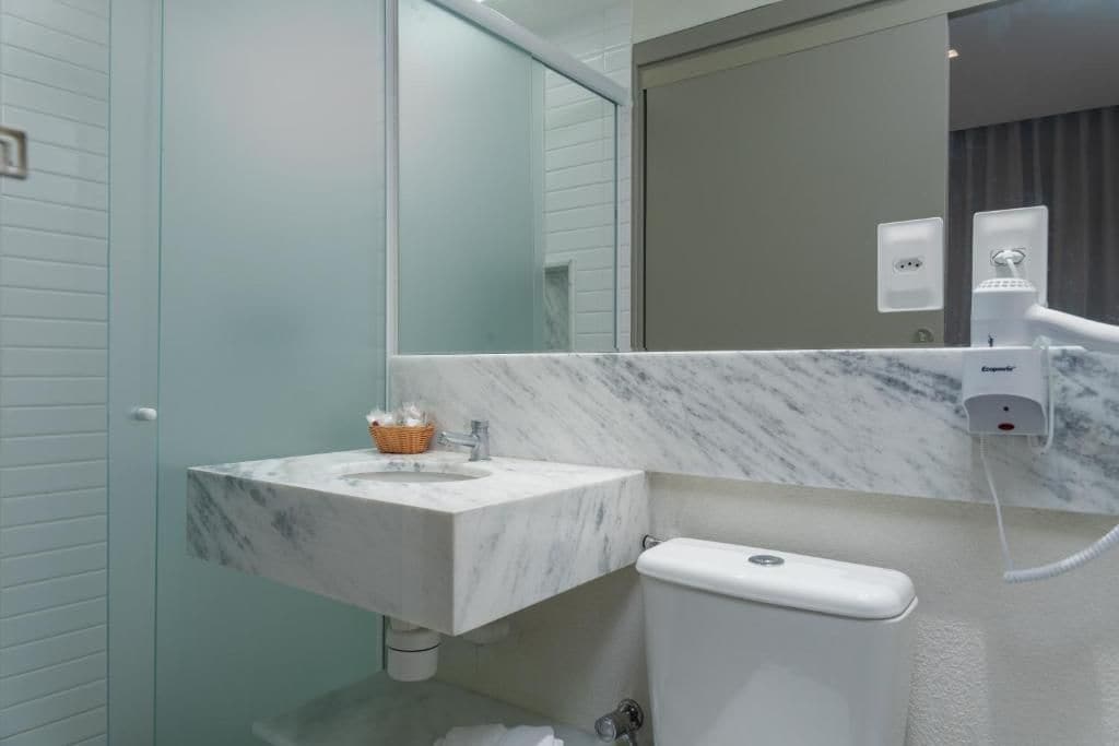 A bathroom with a marble sink, a toilet, a mirror, and a towel rack.