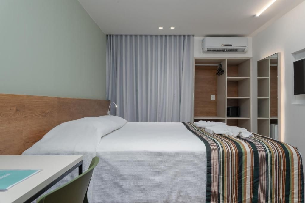 Una habitación de hotel con cama, escritorio, silla, armario y televisor.