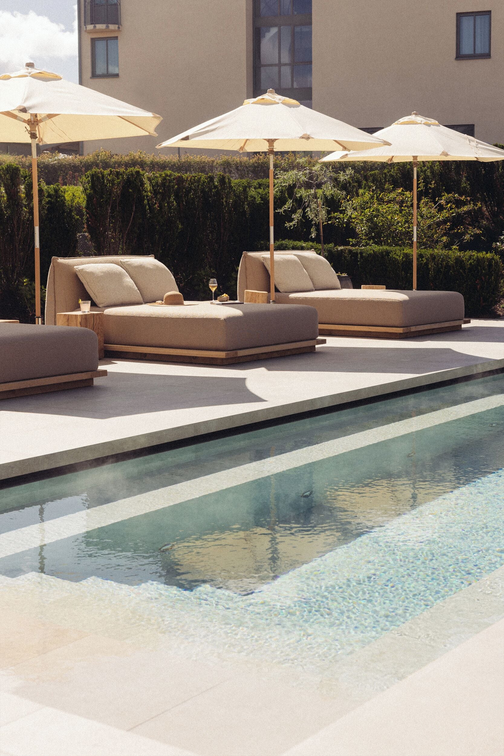 A poolside area with lounge chairs and umbrellas, a pool, and a building in the background.