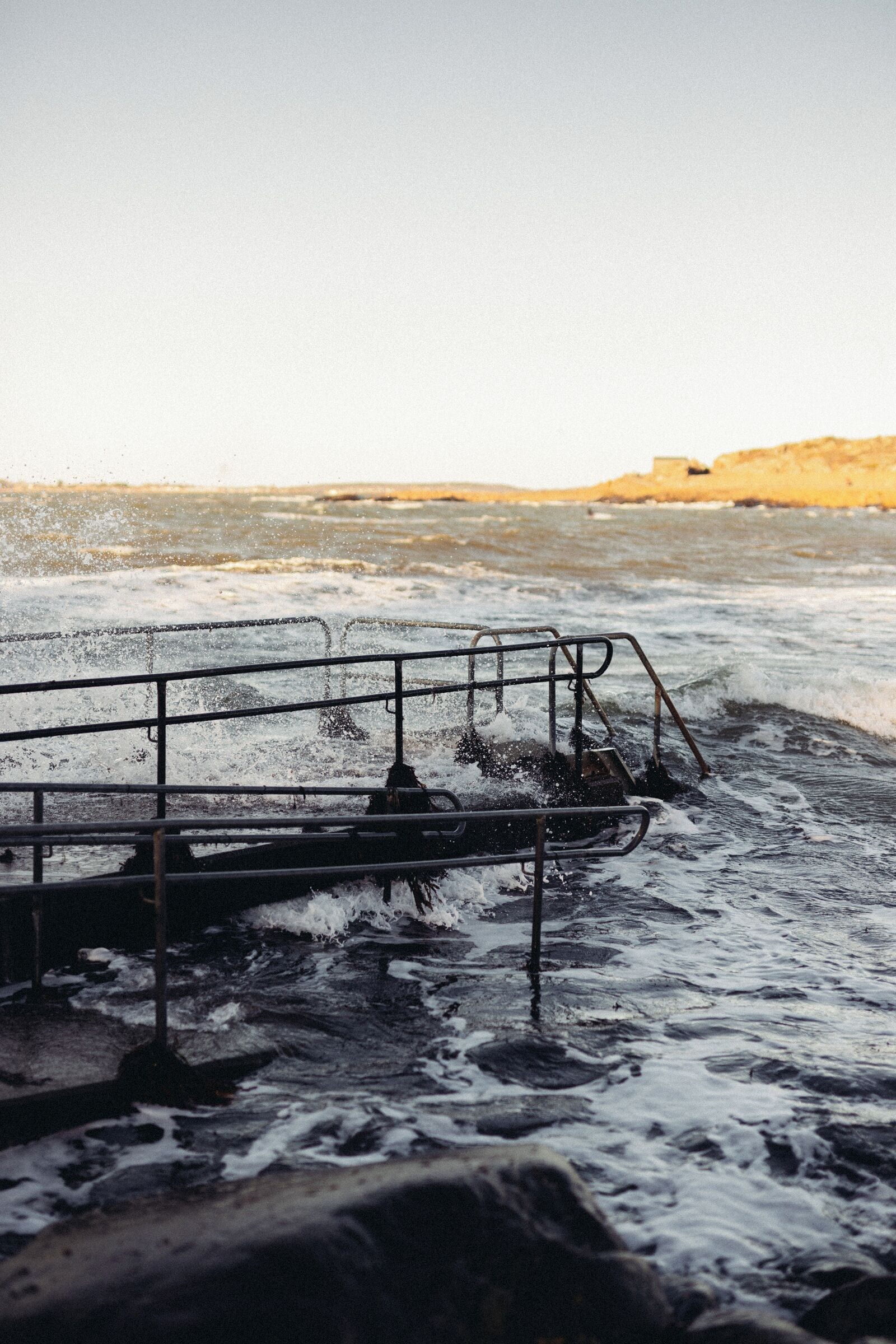 A pier extending into the sea with waves crashing against it.