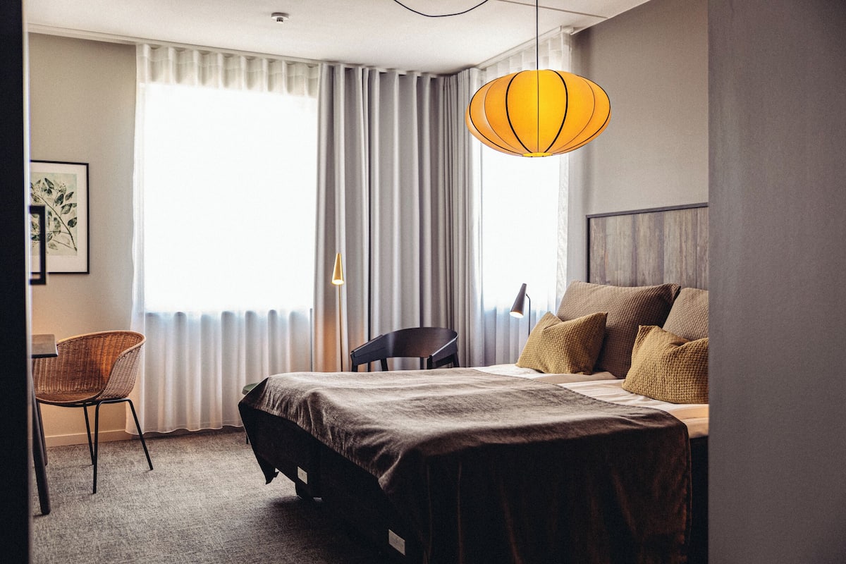 Ein Hotelzimmer mit Bett, Stuhl, Schreibtisch und einem großen Fenster mit Vorhängen.