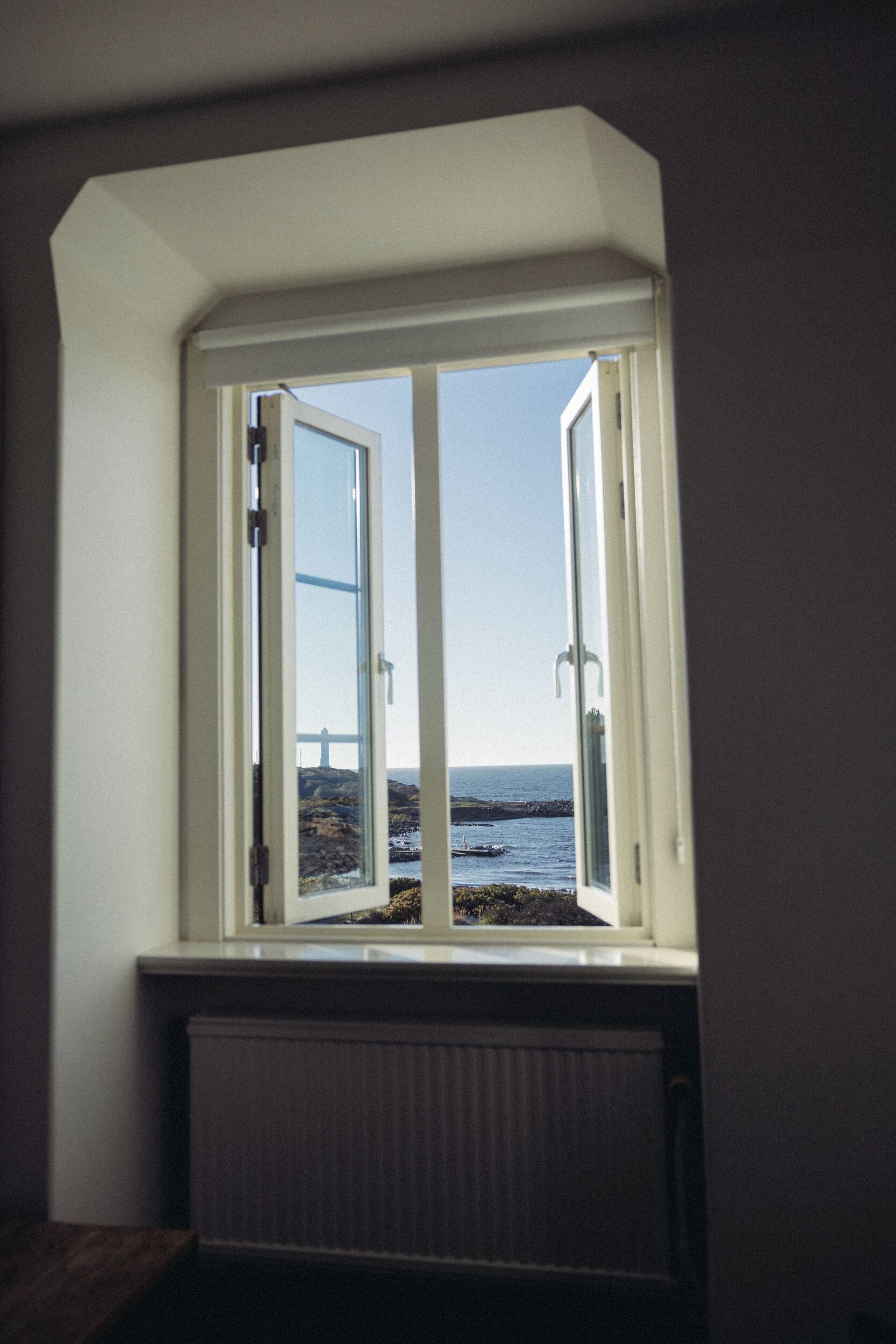 Ein Zimmer mit Erkerfenster, das Blick auf eine felsige Küstenlinie und eine Brücke bietet.