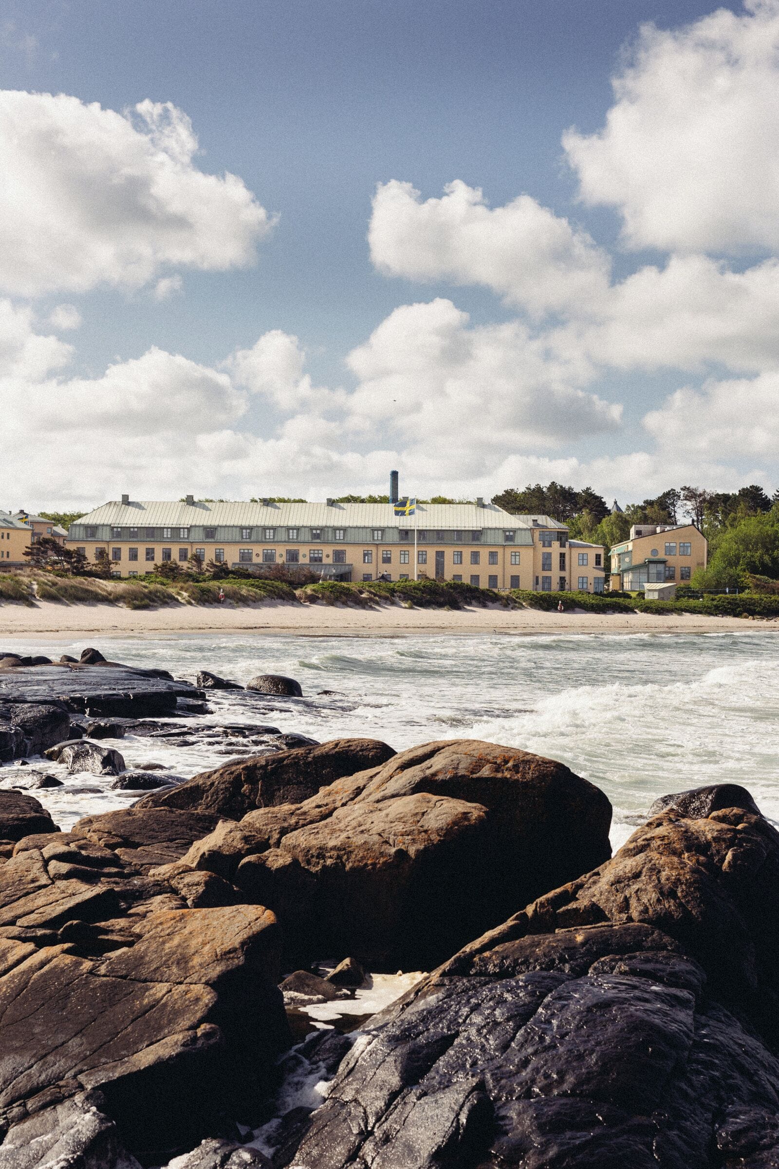 A coastal hotel with a large building, rocky shoreline, and waves.