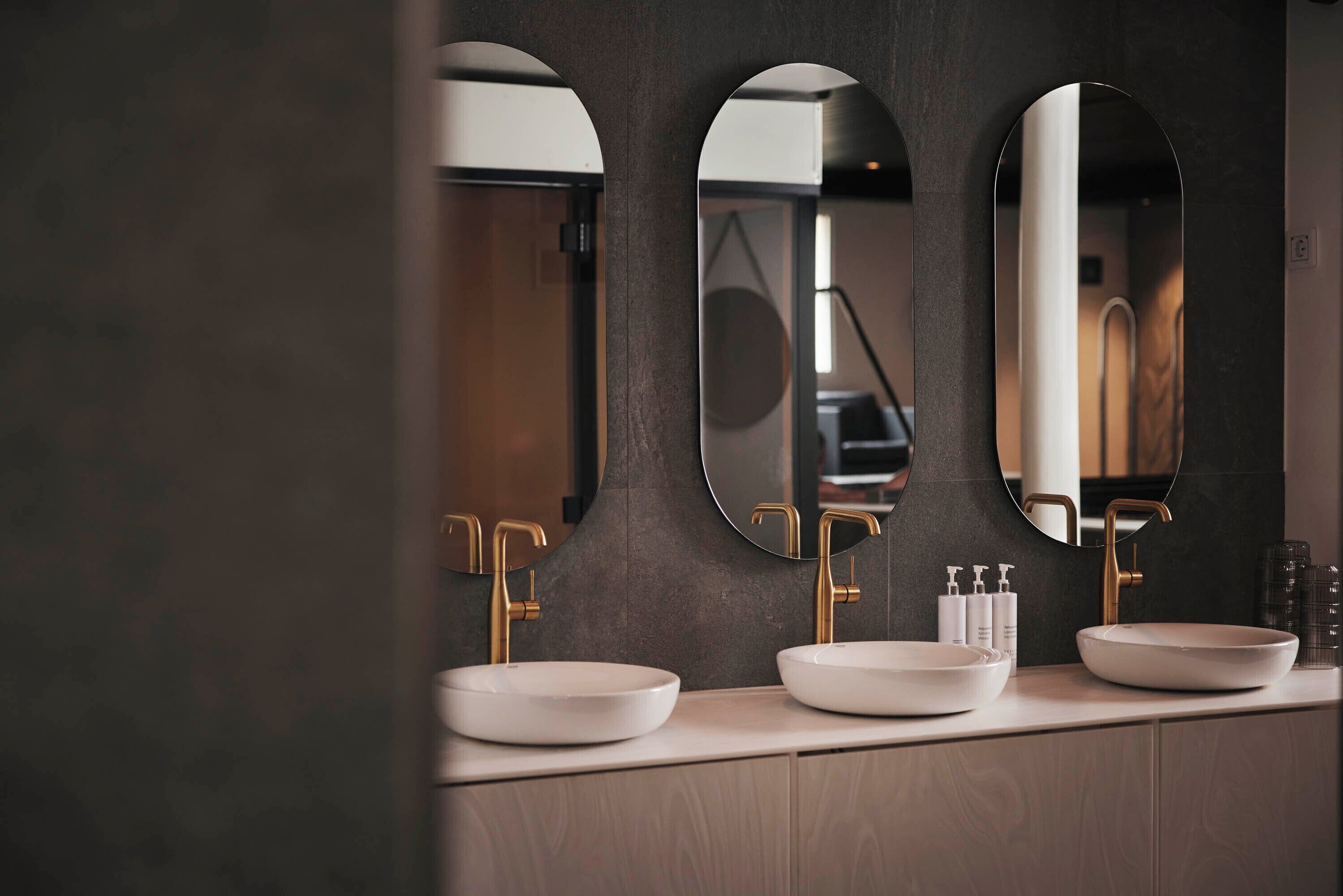 A modern bathroom with two sinks, three mirrors, and a wooden vanity.