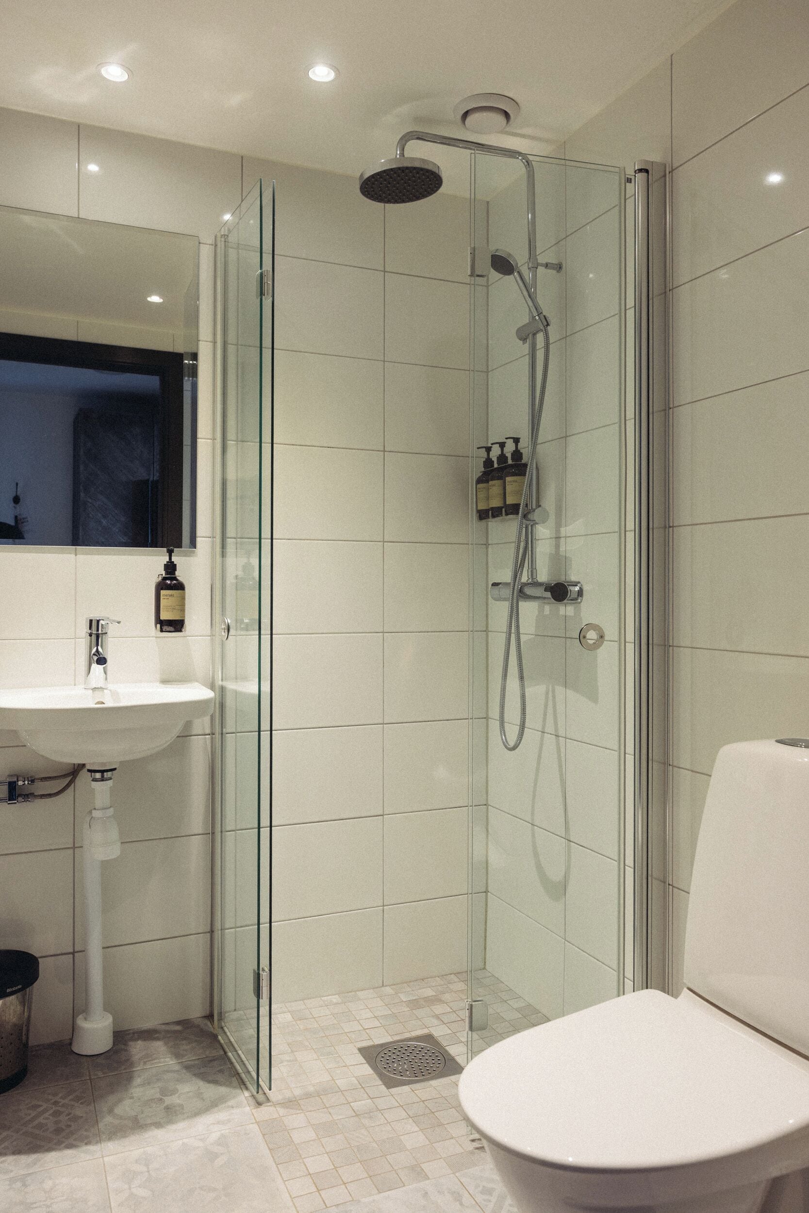 Un baño moderno con ducha de vidrio, lavamanos blanco y retrete.