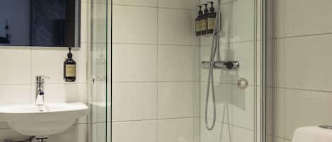 Un baño moderno con ducha de vidrio, lavamanos blanco y retrete.